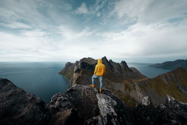 Mann i gul jakke med hette på toppen av fjell
